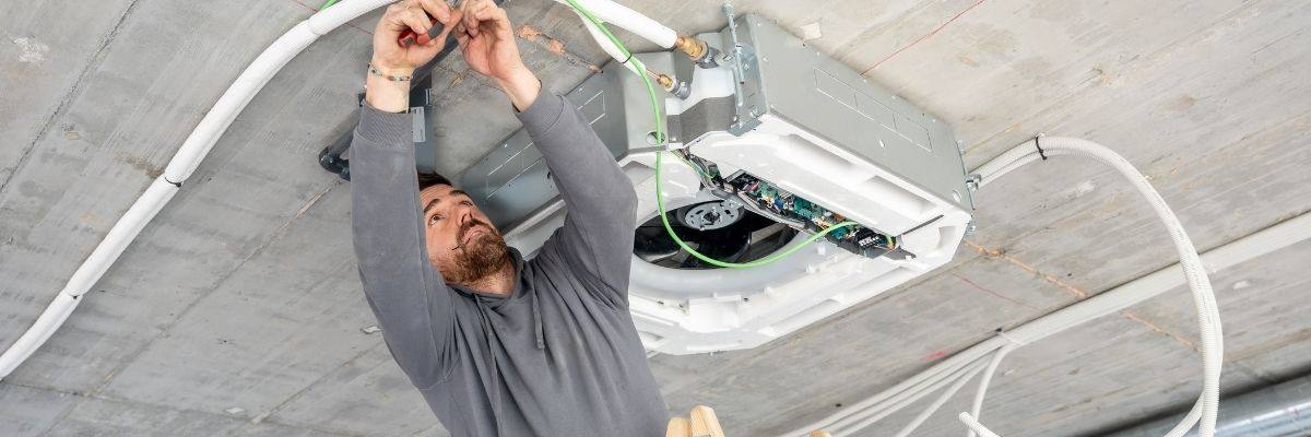 Technician installing a ceiling cassette air conditioner in a commercial building